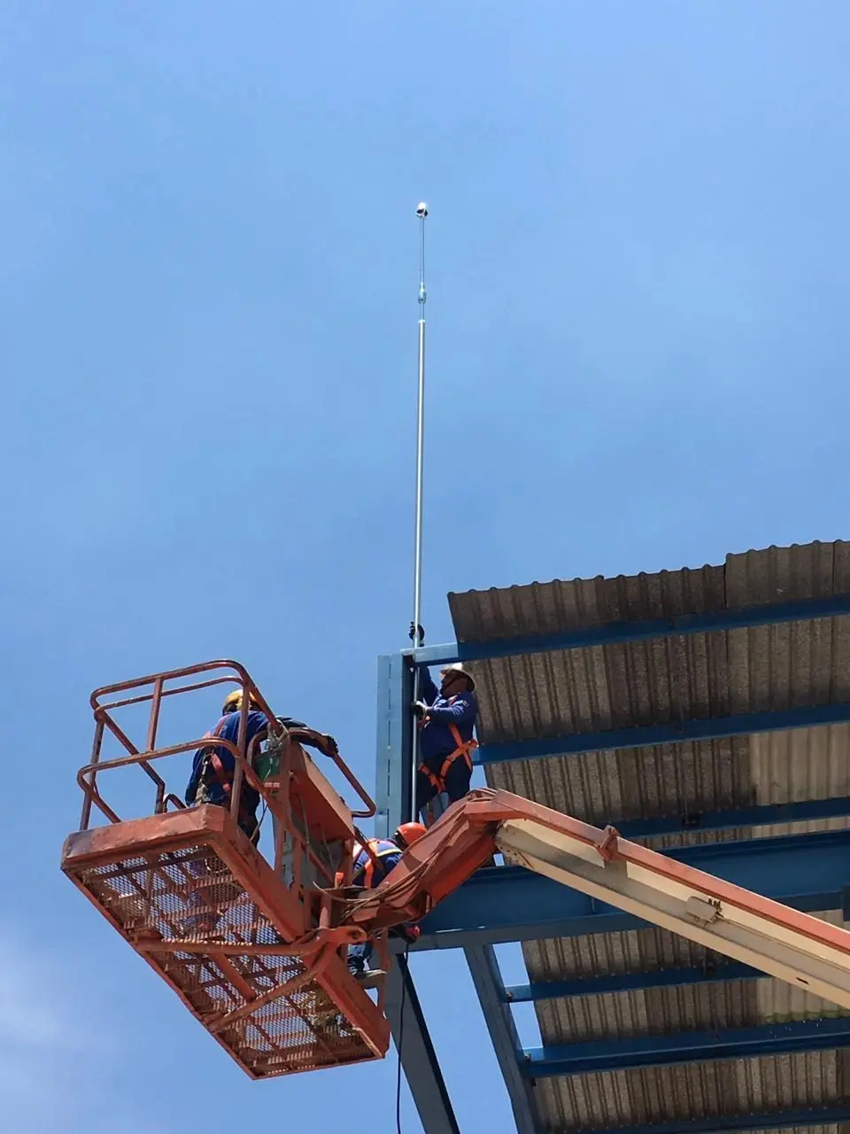 Técnicos en canastilla elevadora instalando un pararrayos en una nave