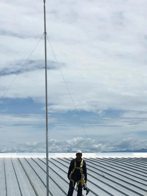 Técnico con equipo de seguridad sobre la lámina de una nave junto al pararrayos